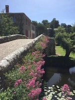 Uma ponte de pedra sobre um canal com flores cor-de-rosa e foles de ninfeia.