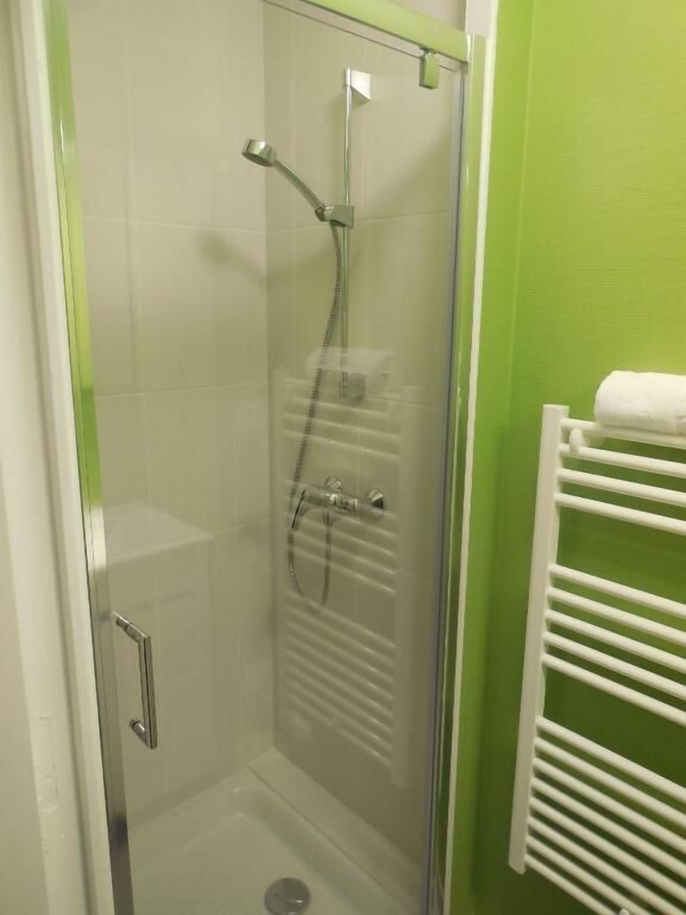 A glass-enclosed shower with a handheld showerhead and a wall-mounted faucet.