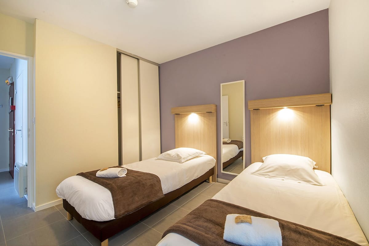 A hotel room with two single beds, a mirror, and a door leading to a hallway.