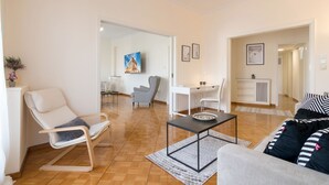 A modern living room with a sofa, a rocking chair, a dining area with a table and chairs, and a kitchen area with a counter and appliances.