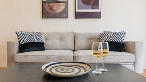 A modern living room with a sofa, two patterned pillows, a black coffee table, a spiral plate, and two glasses of white wine.