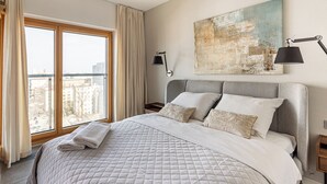 A modern hotel room with a large bed, a city view, a painting on the wall, and a nightstand with a lamp. - Centrum Mennica I (Warsaw)