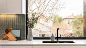 A kitchen counter with a potted plant, a book, and a bottle. - Docker St Elwood Apartments by UrbanRest (Elwood)