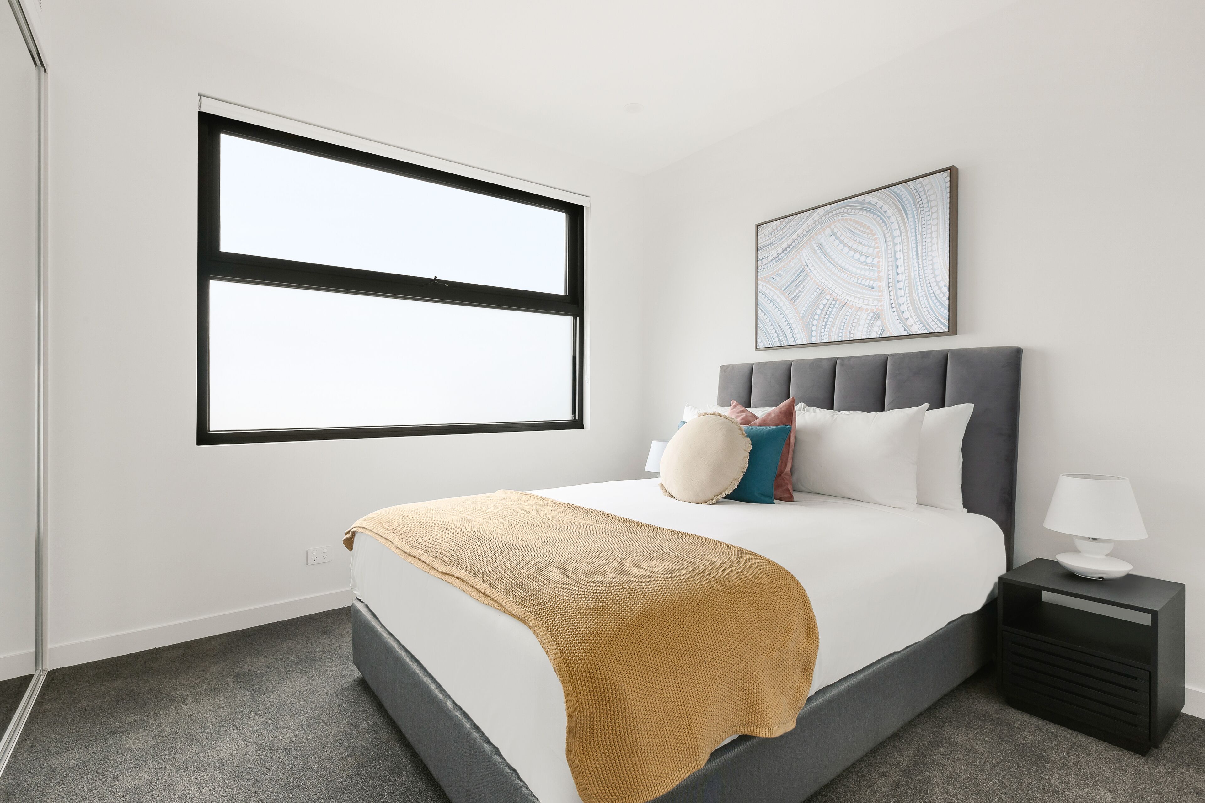 Une chambre moderne avec un grand lit, une table de chevet avec une lampe et une fenêtre avec des stores.