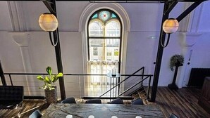 A conference room with a stone table, black chairs, and a view of a staircase leading to a second floor. - La Chapelle du Carmel - Centre Ville - SPA (Reims)
