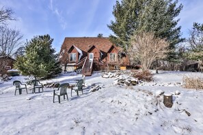 Une maison en bois avec une cheminée en briques, entourée d’un paysage enneigé et d’arbres.