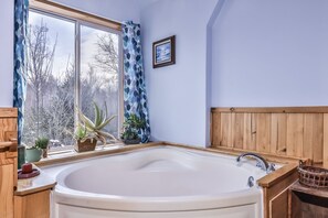 Une salle de bain avec une grande baignoire, un lambris en bois, une fenêtre avec des rideaux bleus et plusieurs plantes en pot.