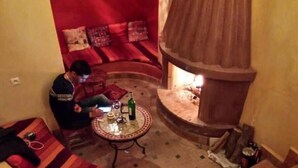 A cozy room with a built-in fireplace, a sofa, and a small table with a bottle and glasses. - 4 Transfert Gratuit Vers le Riad , à Votre Arrivée (Marrakech)