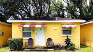 A yellow house with a white door, two Adirondack chairs, a small garden, and a decorative fountain. - A comfortable 1bed 1 bath apartment located in a quit community.  (Lakeland)