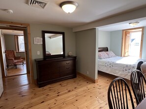 Un dormitorio con un aparador de madera, una cama con ropa de cama estampada y una silla.