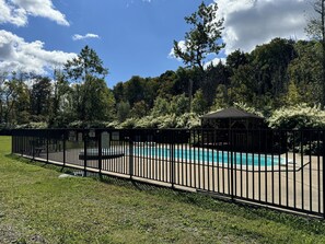 Un área de piscina al aire libre con cerramiento, que incluye un pabellón, rodeada de abundante vegetación y árboles.