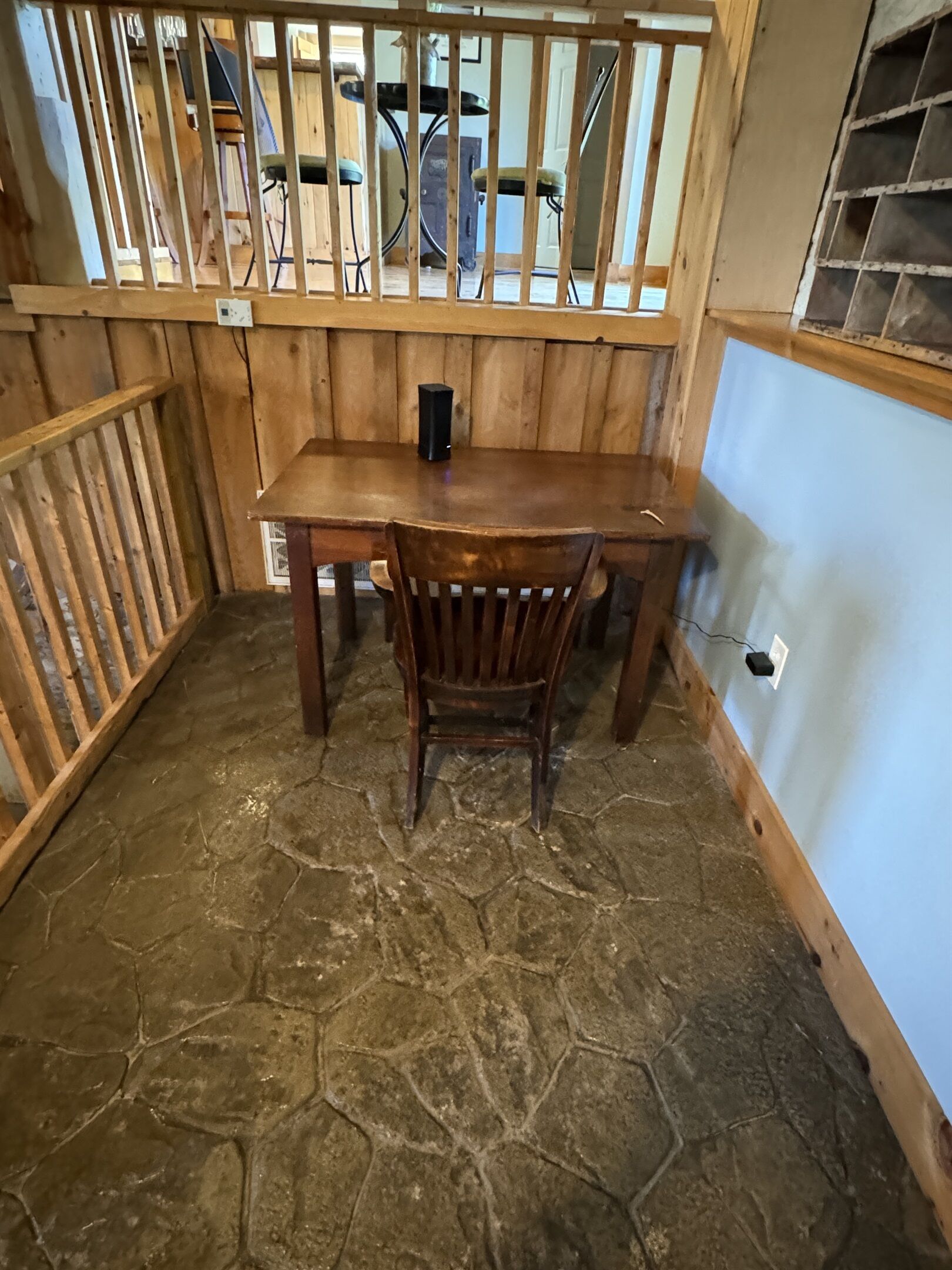 Une table de salle à manger en bois, une chaise, un objet noir posé sur la table et un sol en pierre.
