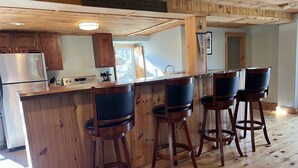 Ett kök med träskåp, ett kylskåp i rostfritt stål, en bardisk med fyra barstolar och en skylt ovanför bardisken med texten: ”Lev väl, skratta ofta, älska mycket”.
