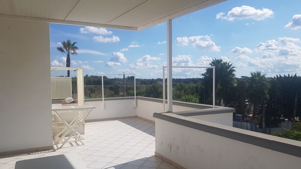 A balcony with a table and chairs, a view of the sky and clouds, and a distant landscape. - Trilocale Mimose in Baia Verde (Gallipoli)