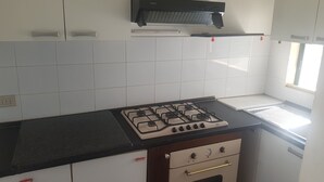 A kitchen with white cabinets, a gas stove, a built-in oven, and a black countertop. - Trilocale Mimose in Baia Verde (Gallipoli)