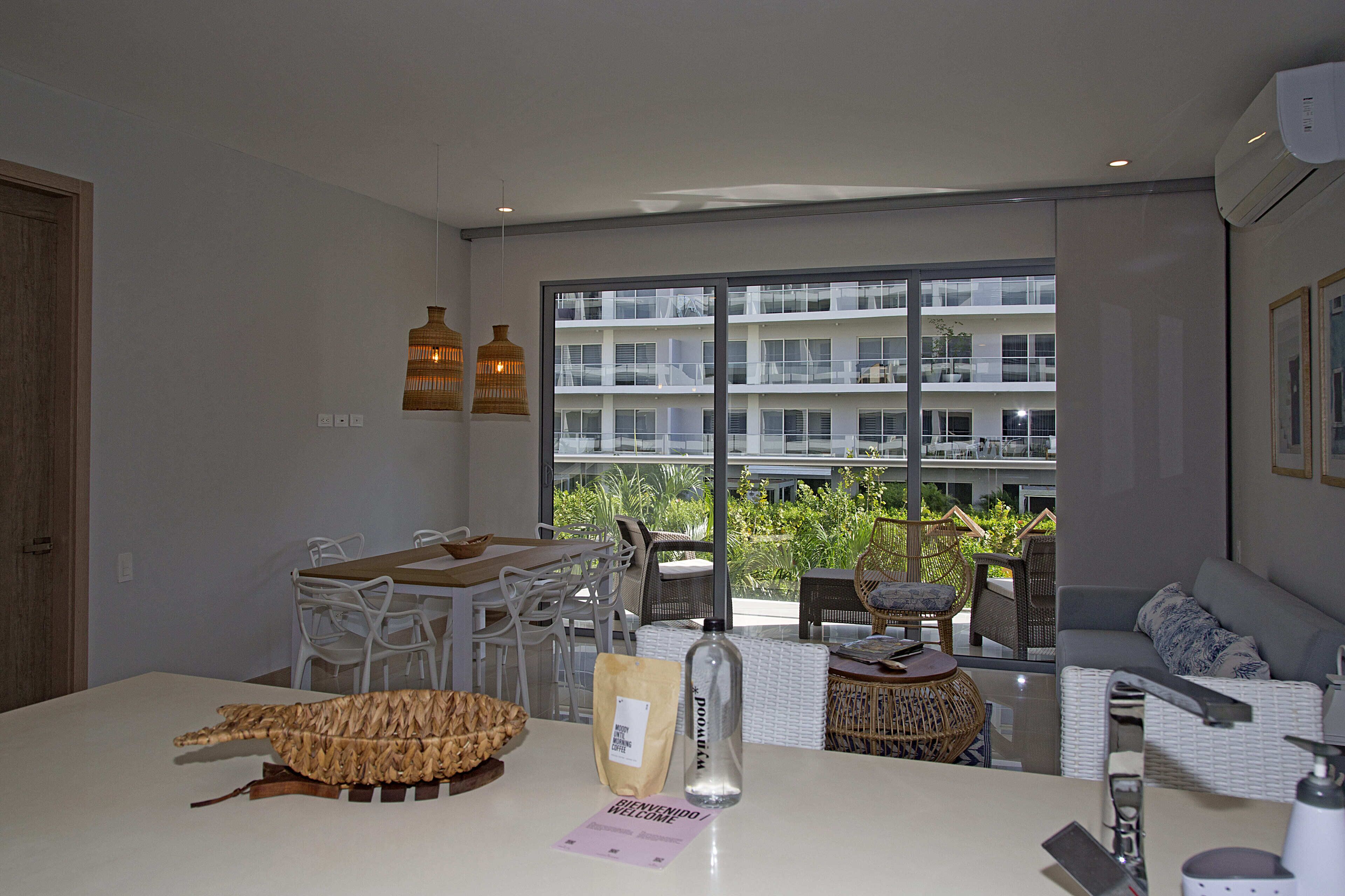 A modern living room with a dining area, large windows, and a view of a building.