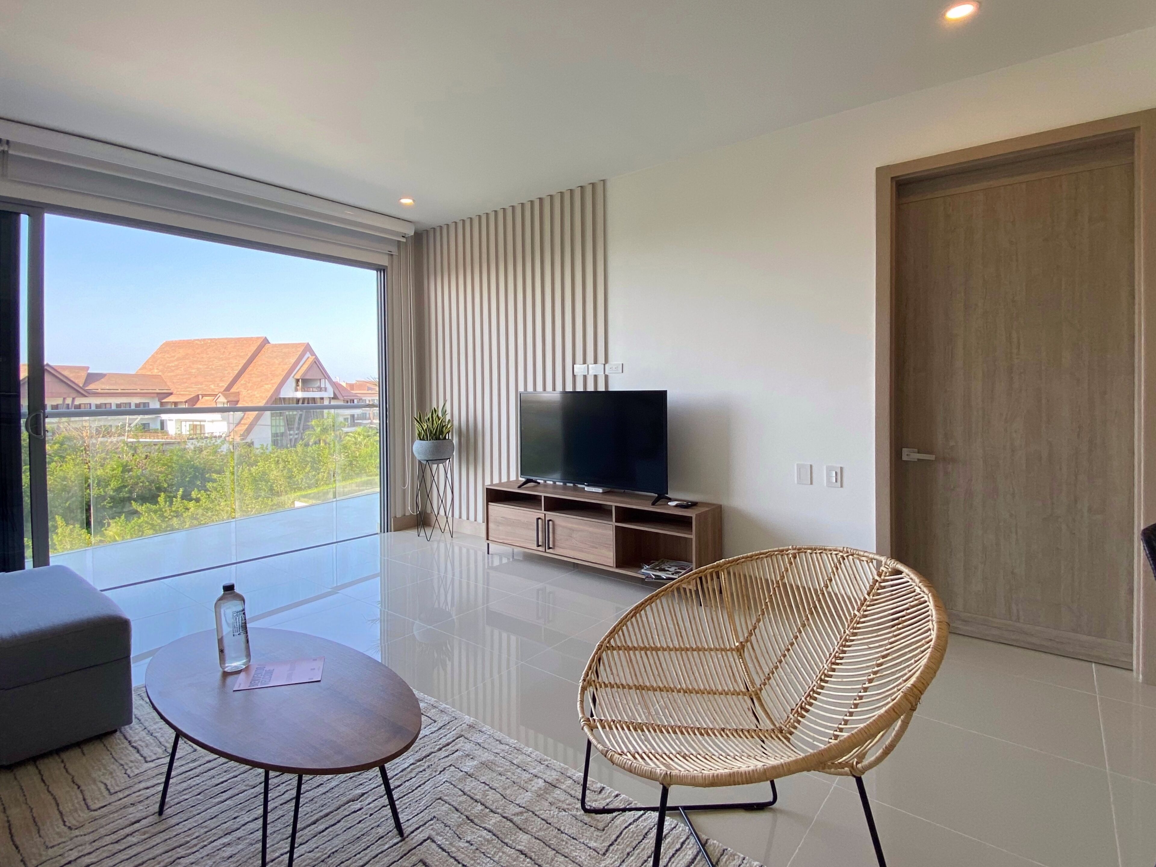 Una sala de estar moderna con un ventanal grande, un televisor de pantalla plana, un sillón de mimbre y una mesita.