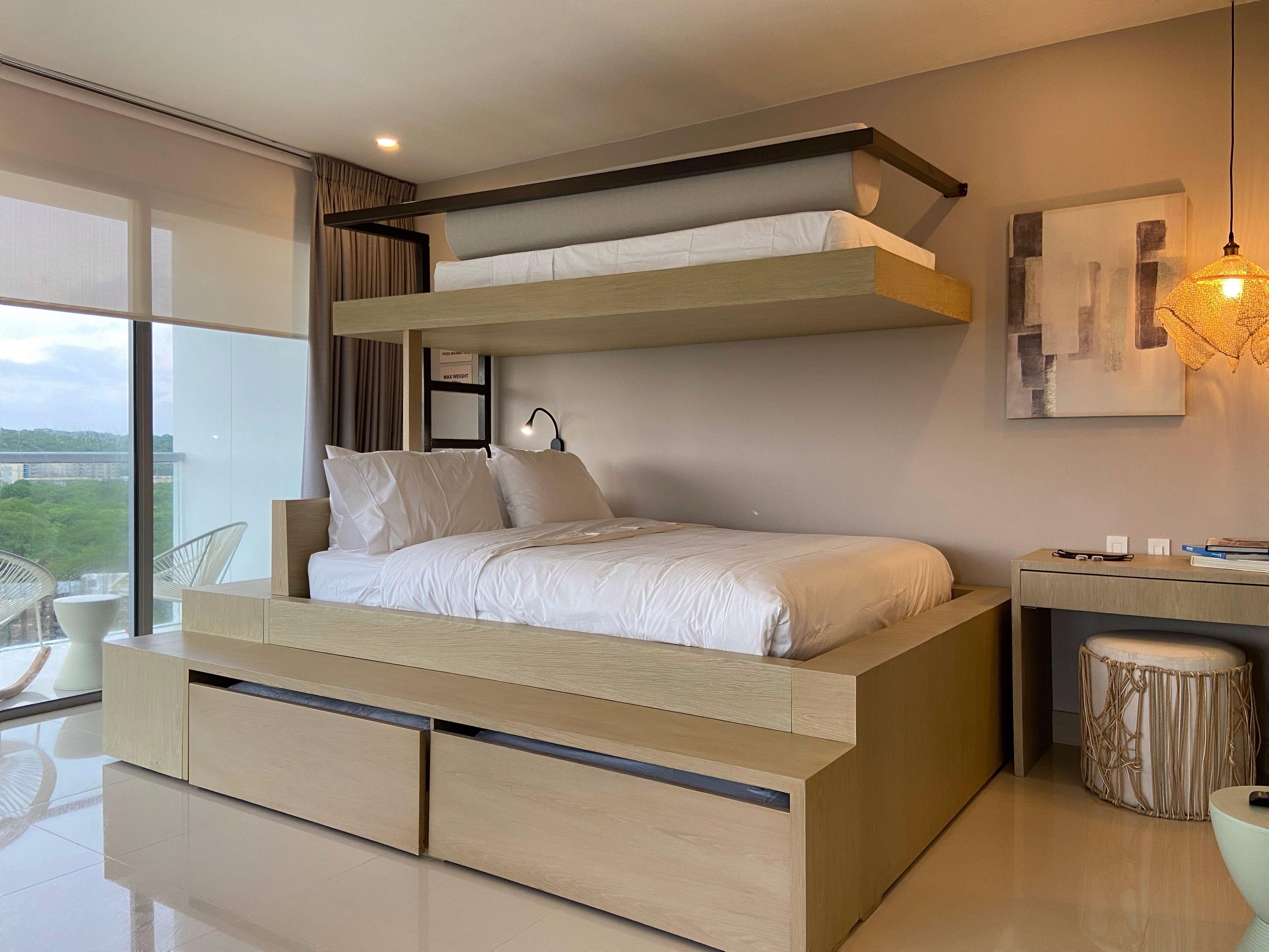 Ein modernes Schlafzimmer mit Etagenbett, Nachttisch, Lampe und Blick auf die Stadt.