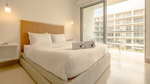 A modern hotel room with a large bed, a wooden headboard, a balcony with a view of buildings, and a white color scheme. - Eco by Wynwood House (Cartagena)