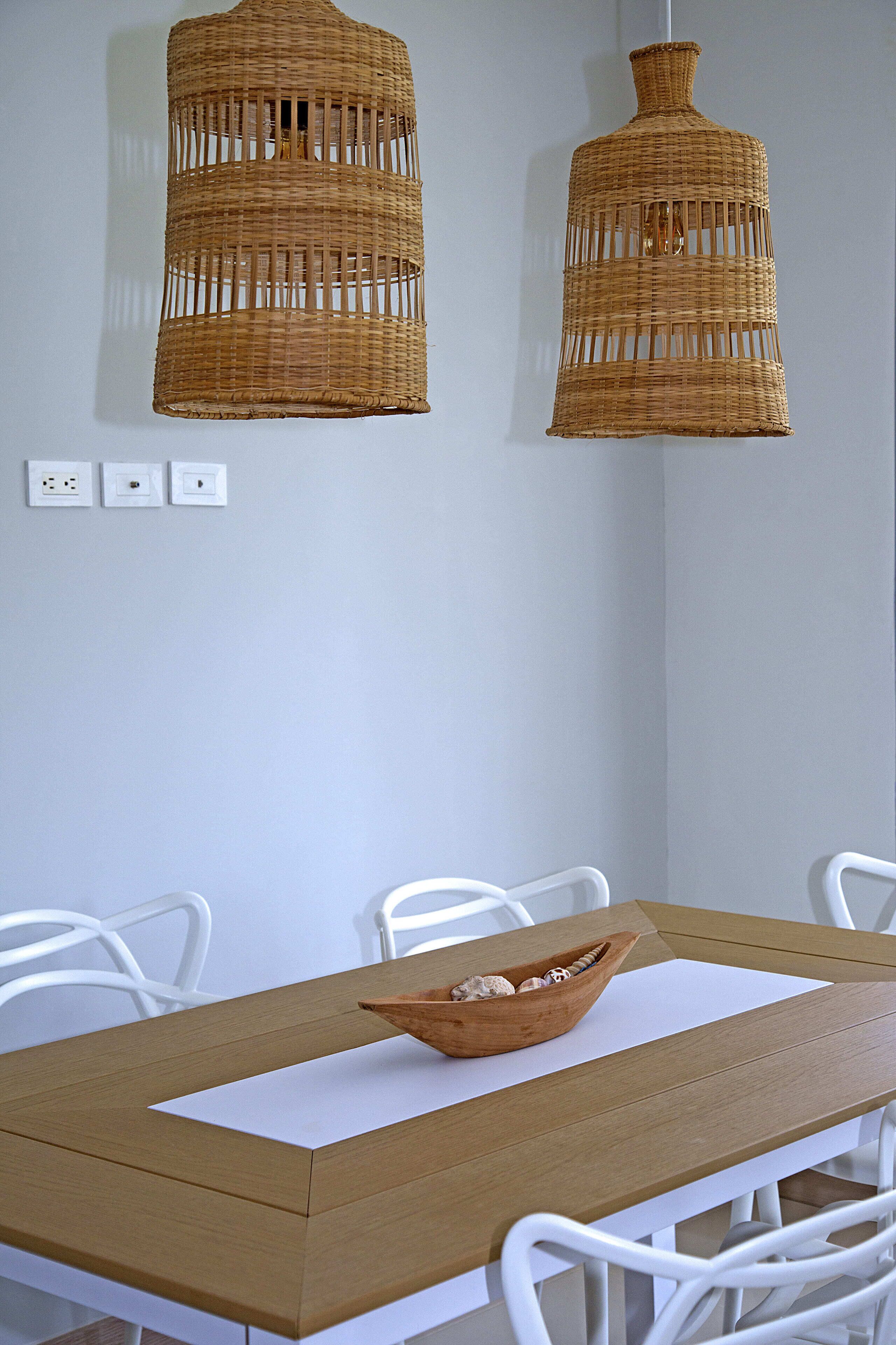 A dining area with a wooden table, white chairs, and two wicker pendant lights.