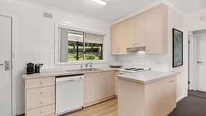 Una cocina moderna con armarios blancos y de madera clara, un lavamanos de acero inoxidable y una ventana con vistas a un jardín.