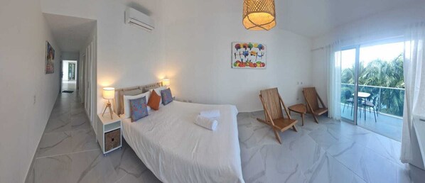 Ein geräumiges Schlafzimmer mit einem großen Bett, einem Balkon mit Sitzgelegenheiten und Blick auf Palmen.