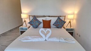 Una cama bien hecha con sábanas blancas y dos almohadones decorativos, uno naranja y dos con un estampado floral azul.