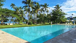 Una piscina rectangular con agua azul cristalina, rodeada por un patio de concreto y una zona verde con palmeras.