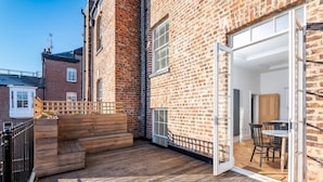 Una casa in mattoni con un patio in legno, una porta scorrevole in vetro che dà su un'area pranzo e una piccola scala.