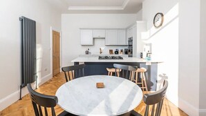 Una cucina moderna con mobili bianchi, un'isola centrale e un'area pranzo con tavolo e sedie in marmo.