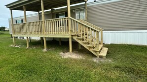 A wooden deck with a staircase leading to a covered porch of a single-story house.