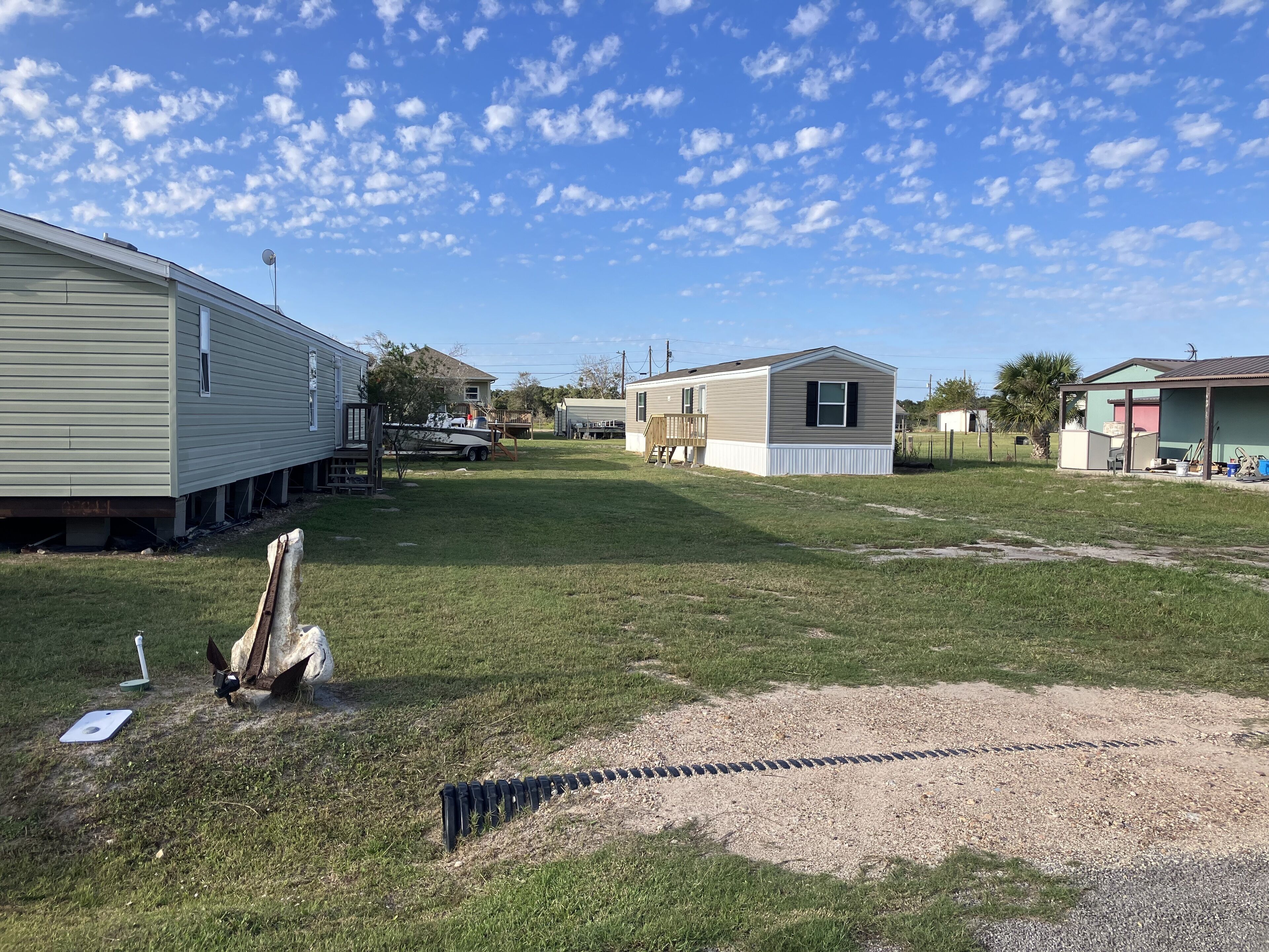 A residential area with mobile homes, a grassy yard, and a gravel path.