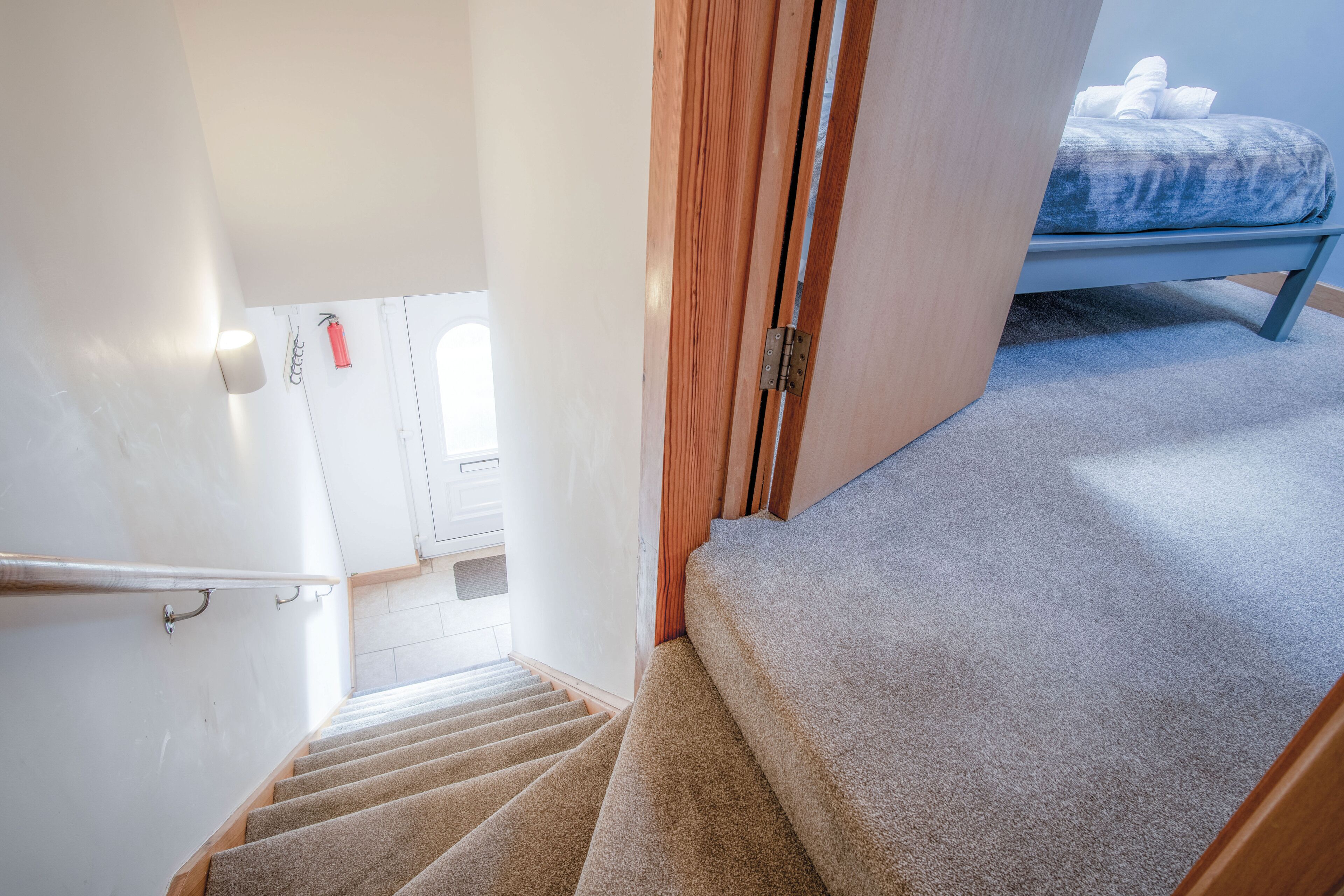 A carpeted staircase leading to a bedroom with a bed and a wooden door.