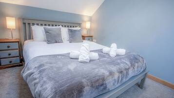 A neatly made bed with a grey blanket and pillows, two bedside tables with lamps, and a wooden bench at the foot of the bed.