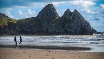 A beach with rocky cliffs and two people walking along the shore.
