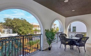 A balcony with a glass table and chairs, surrounded by white arches and a metal railing. - Ocean View Home with Pool in Gated Community - 1 Min Walk to Ocean (Destin)