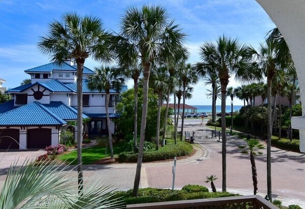 A residential area with a house featuring a blue roof, palm trees, and a view of the ocean. - Ocean View Home with Pool in Gated Community - 1 Min Walk to Ocean (Destin)