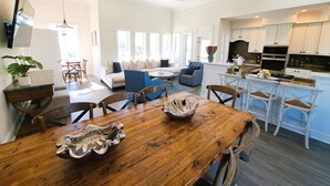 Een moderne keuken met witte kasten, een eethoek met een houten tafel en een zithoek met een bank en stoelen.
