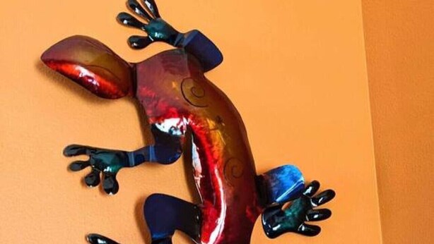 Una escultura de gecko sobre un fons taronja uniforme.