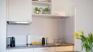 A modern kitchen with white cabinets, a stainless steel range hood, a built-in sink, and a countertop with a coffee machine and a plate of lemons. - Apartment Bianca Superior (Salzburg)