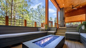 Un espacio moderno al aire libre con zona de estar, una chimenea integrada y un deck de madera, además de una chimenea de piedra.