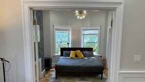 A bedroom with a bed, two windows, a chandelier, and a herringbone-patterned rug. - Have a Spring Fling or Work Remote - Hi Speed  WIFI! (Chicago)