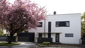 Un bâtiment moderne à deux étages, doté d’un toit plat, d’un garage et d’un petit jardin agrémenté d’un arbre.