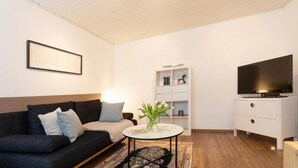 Un salon moderne avec un canapé gris foncé, une table d’appoint blanche, un téléviseur à écran plat et un meuble blanc avec des étagères.