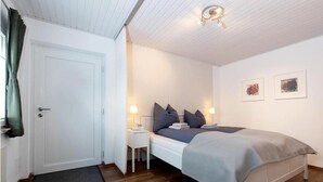 Une chambre à coucher avec un lit, des tables de chevet, une porte et un luminaire au plafond.