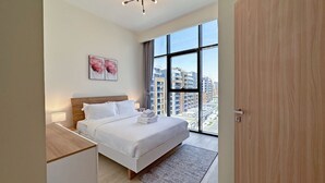 Un dormitorio moderno con un ventanal grande, una cama con sábanas blancas, una mesita de noche y un cuadro en la pared.