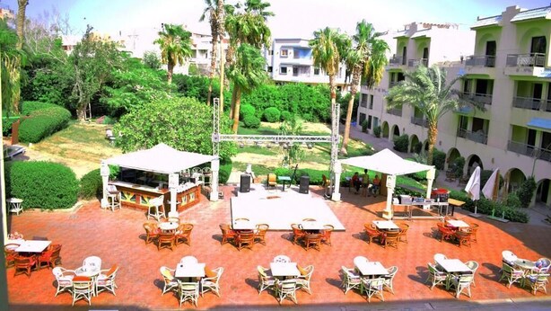 An outdoor patio area with multiple tables and chairs, surrounded by palm trees and greenery. - Single Room LA
الغردقه
ميدان المحمدي الهضبه اول الممشى السياحي
 (Hurghada)
