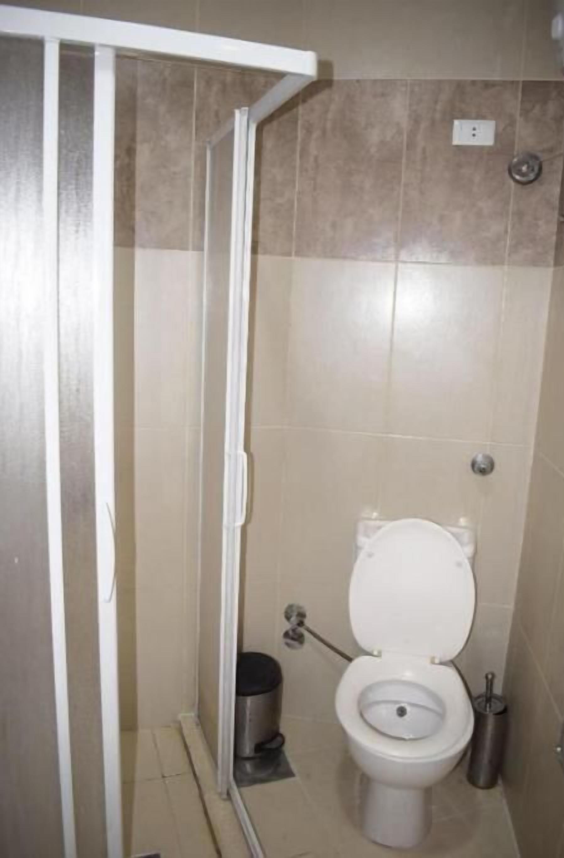 Une salle de bain équipée de toilettes, d’une poubelle et d’un espace douche.