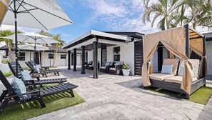 Een moderne buitenlounge met ligbedden, een overdekte zithoek en een hemelbed.