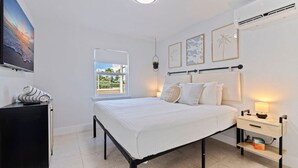 A bedroom with a bed, bedside tables, a TV, and a window with a view. - Las Olas of Treasure Island No. 1 (Treasure Island)
